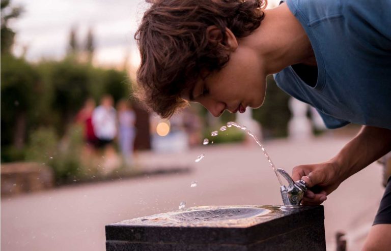 Junger Mann trinkt bei großer Hitze aus einem öffentlichen Brunnen